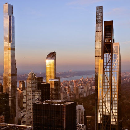 City skyline at sunset featuring tall modern skyscrapers and a view of a river in the distance.