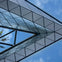 Glass and metal architectural structure with a reflective surface against a blue sky with scattered clouds.