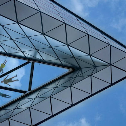 Glass and metal architectural structure with a reflective surface against a blue sky with scattered clouds.