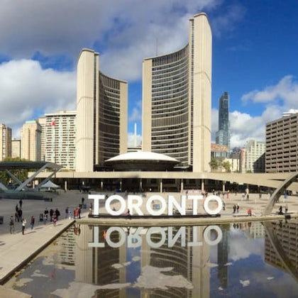 People walk around Toronto's City Hall with a large "TORONTO" sign and reflecting pool in the foreground.