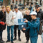 A group of people in casual clothing gathered outdoors, smiling and looking at a blue box held by a person in a blue jacket.