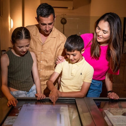 Two adults and two children looking at a display table in a museum or exhibit hall.