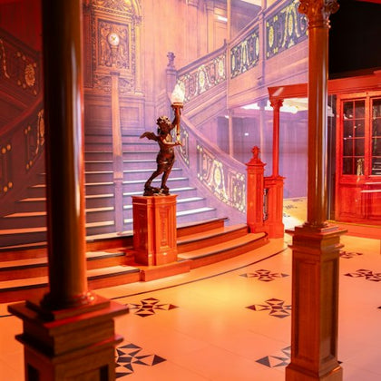 A detailed replica of the Titanic's grand staircase, featuring ornate woodwork, a cherub statue, and elegant lighting.