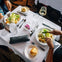Two people having a meal at a restaurant table with salads, bread rolls, water, wine, and silverware on a white tablecloth.