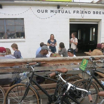 People sitting and standing outside "Our Mutual Friend Brewery," with bicycles parked in the foreground.