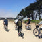 A group of people riding bicycles on a gravel path next to trees under a clear blue sky.