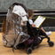 A child in a stroller draws on a clipboard, covered by a transparent rain cover.