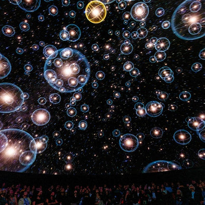 A planetarium show featuring a starry sky with bubble-like visuals projected on the dome above an audience.