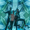 Four people are posing energetically in front of an illuminated background with intricate, symmetrical neon patterns.
