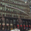 Street view of a building with many windows, a Staples store on the ground level, and a car passing by in the foreground.