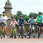 A group of five people, including children, standing with bicycles on a decorative stone bridge on a sunny day.