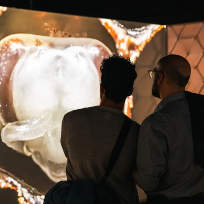 Two people stand in front of a large illuminated display showing a magnified close-up of a biological structure.