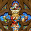 A stained glass window featuring a religious scene with figures, angels, and vibrant colors in an ornate design.