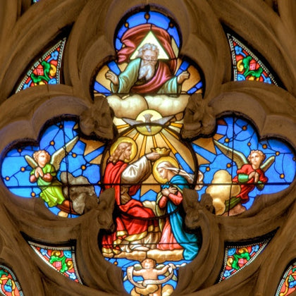A stained glass window featuring a religious scene with figures, angels, and vibrant colors in an ornate design.