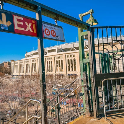 Exit sign and stairs leading down from a platform with Yankee Stadium in the background under a clear blue sky.