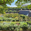 A formal garden with intricate hedges forming a spiral maze, surrounded by lush greenery and a waterfall in the background.