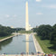 The Washington Monument reflected in the Reflecting Pool, with the U.S. Capitol in the background and visitors nearby.
