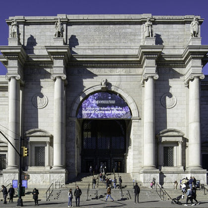 People walking in front of a large classical-style building with columns and an arched entrance, featuring a banner above the doorway.