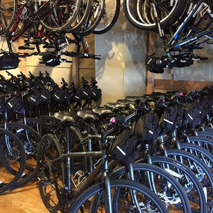 A room filled with bicycles, including rows of parked bikes and additional bikes hanging from racks above.