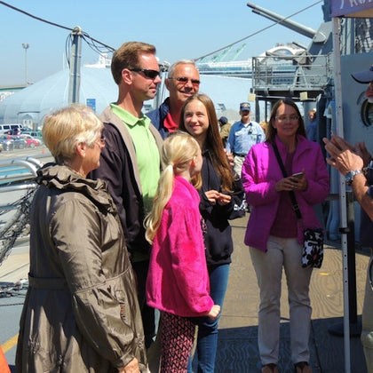 A group of people standing on a ship deck, some wearing jackets. Background includes a dome structure and other ship machinery.