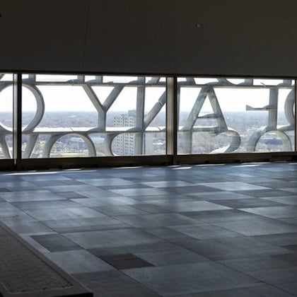Interior view of a modern building with large windows featuring decorative text and a cityscape in the background.