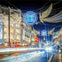 A bustling city street at night with illuminated festive decorations, including angel wings and glowing spheres, above the road.