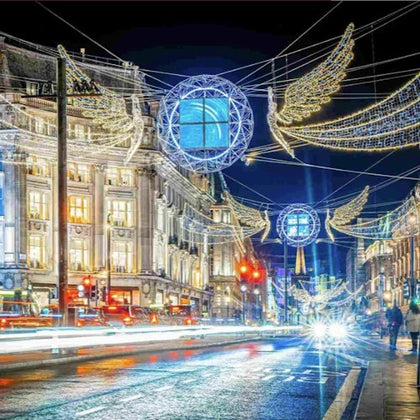 A bustling city street at night with illuminated festive decorations, including angel wings and glowing spheres, above the road.