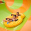 Two children smiling while riding a yellow inflatable raft down a water slide with orange and green sections.