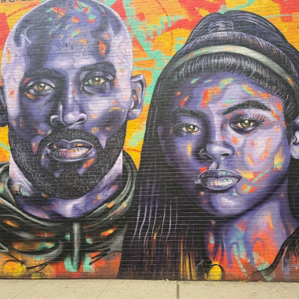 Colorful mural on a brick wall featuring two vibrant, purple-toned faces against an abstract, multicolored background.