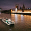 A boat sails on a river at night with the illuminated British Parliament building in the background.