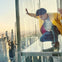 A person crouches on a glass balcony high above a cityscape, surrounded by skyscrapers and a clear sky.