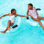Two children in swimsuits float on inflatable rings in a pool, smiling and holding hands.
