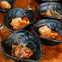 Black bowls containing food garnished with bread slices and skewers are arranged on a wooden table.
