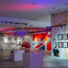 A modern art gallery with framed artworks, a red phone booth, and colorful lights illuminating the space.