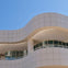 A modern building with curved, white-tiled architecture against a clear blue sky. Rounded windows and columns are also visible.