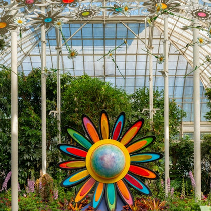 A colorful flower sculpture in a greenhouse with plants and hanging flower decorations.