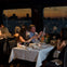 People dining at a restaurant by a window with a sunset cityscape view, engaging in conversation and examining menus.