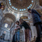A group of people standing inside a large ornate building with a decorated dome ceiling and intricate architectural details.