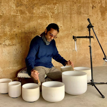 A person playing white ceramic bowls with mallets in a rustic indoor setting, next to a microphone stand.