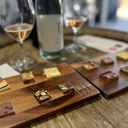 Small dessert squares arranged on wooden boards, accompanied by two glasses of rosé and a bottle on a wooden table.