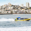 A yellow speedboat with passengers speeding on water, with a city skyline in the background.