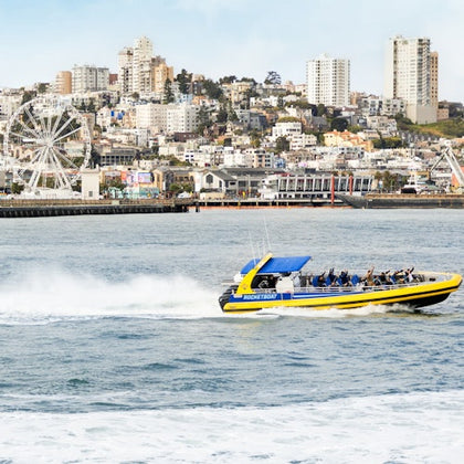 A yellow speedboat with passengers speeding on water, with a city skyline in the background.