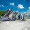 A large sculpture made of colorful graffiti-covered materials, resembling a reclining figure, displayed in an outdoor urban area.