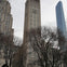 A tall clock tower surrounded by leafless trees and other buildings under an overcast sky.