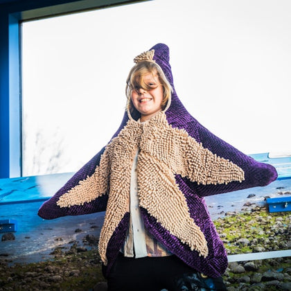 A smiling child wearing a starfish costume at an indoor location with a scenic backdrop of a shoreline.