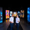 Two people in uniform stand in a hallway with colorful movie-themed panels and a Warner Bros. logo in the background.