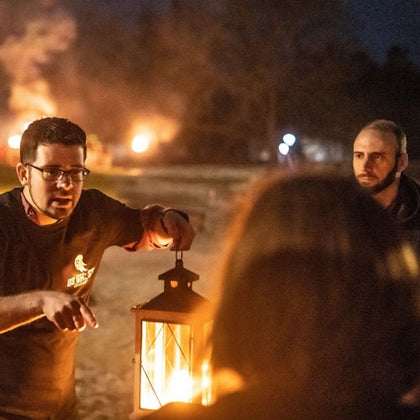 Tour guide telling ghost stories to his group while holding a lantern