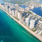Aerial view of a coastal city with high-rise buildings along a sandy beach and turquoise ocean.