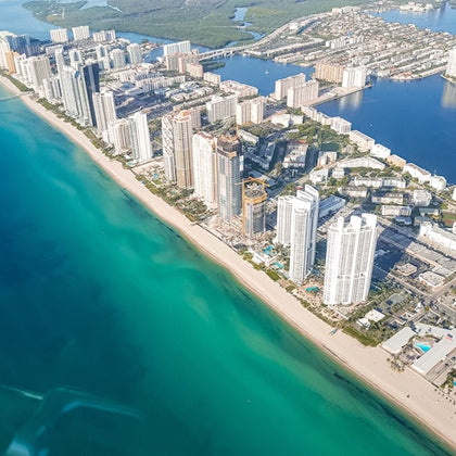 Aerial view of a coastal city with high-rise buildings along a sandy beach and turquoise ocean.