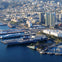 Aerial view of a coastal city with tall buildings, harbor, docked ships, and waterfront buildings.